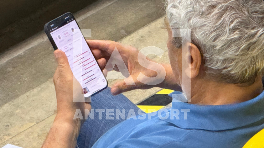 Mircea Lucescu, în tribune la FCSB - Drita, în timp ce verifica rezultatul de la meciul lui PAOK / FOTO: AntenaSport